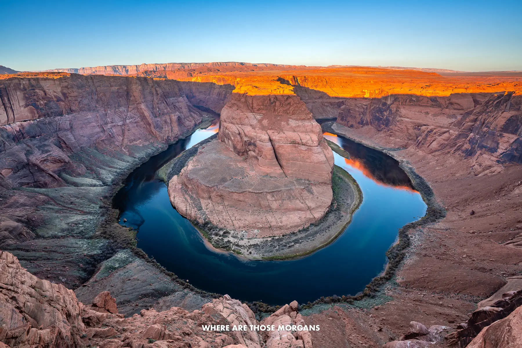 Wide angle photo of Horseshoe Bend at sunrise with sunlight glowing on the landscape above the canyon