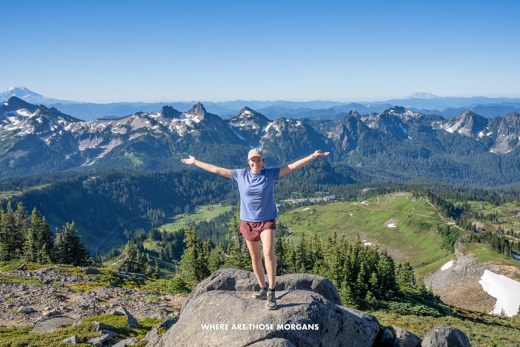 Kristen from Where Are Those Morgans with arms stretched out on a rocky outcrop with wide open views of mountain peaks and volcanoes in Washington State