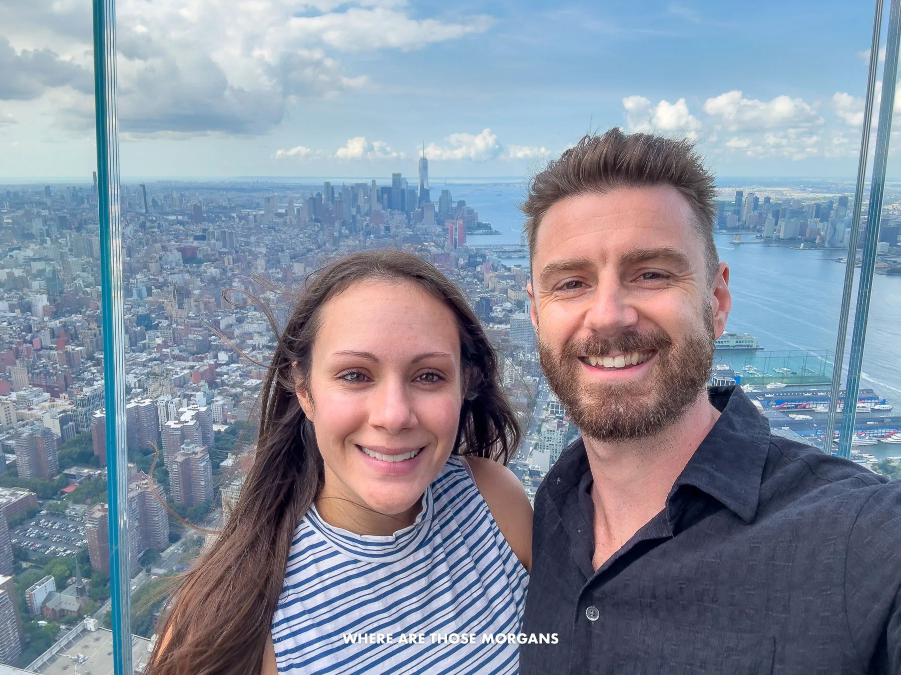 Photo of Mark and Kristen Morgan from Where Are Those Morgans taking a selfie at the top of Edge in NYC with views over the city behind a glass panel