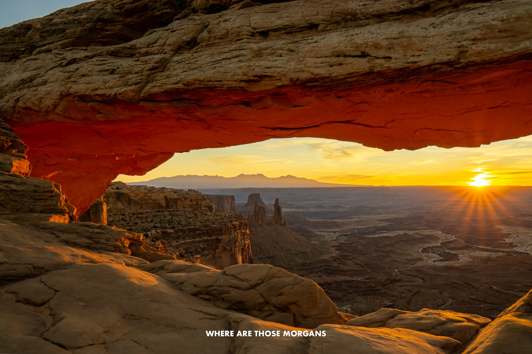 Starburst through a natural sandstone arch and behind a red rock canyon landscape at Mesa Arch