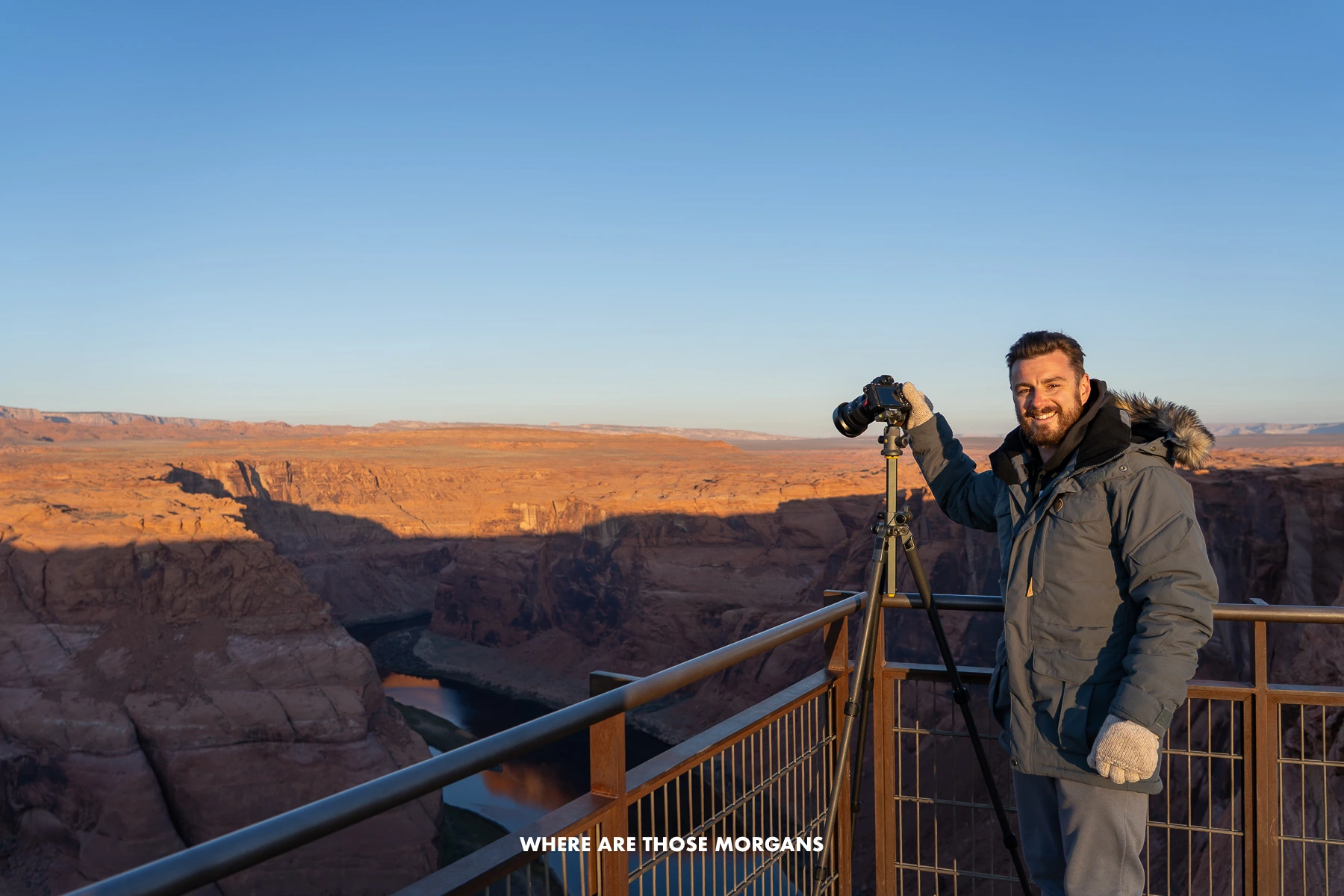 Mark from Where Are Those Morgans in a winter coat with gloves taking a photo on a tripod over a metal fence at a red rock landscape