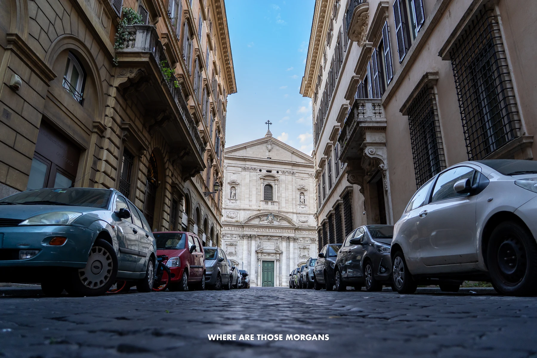 Church at the end of a cobbled road with cars parked on either side