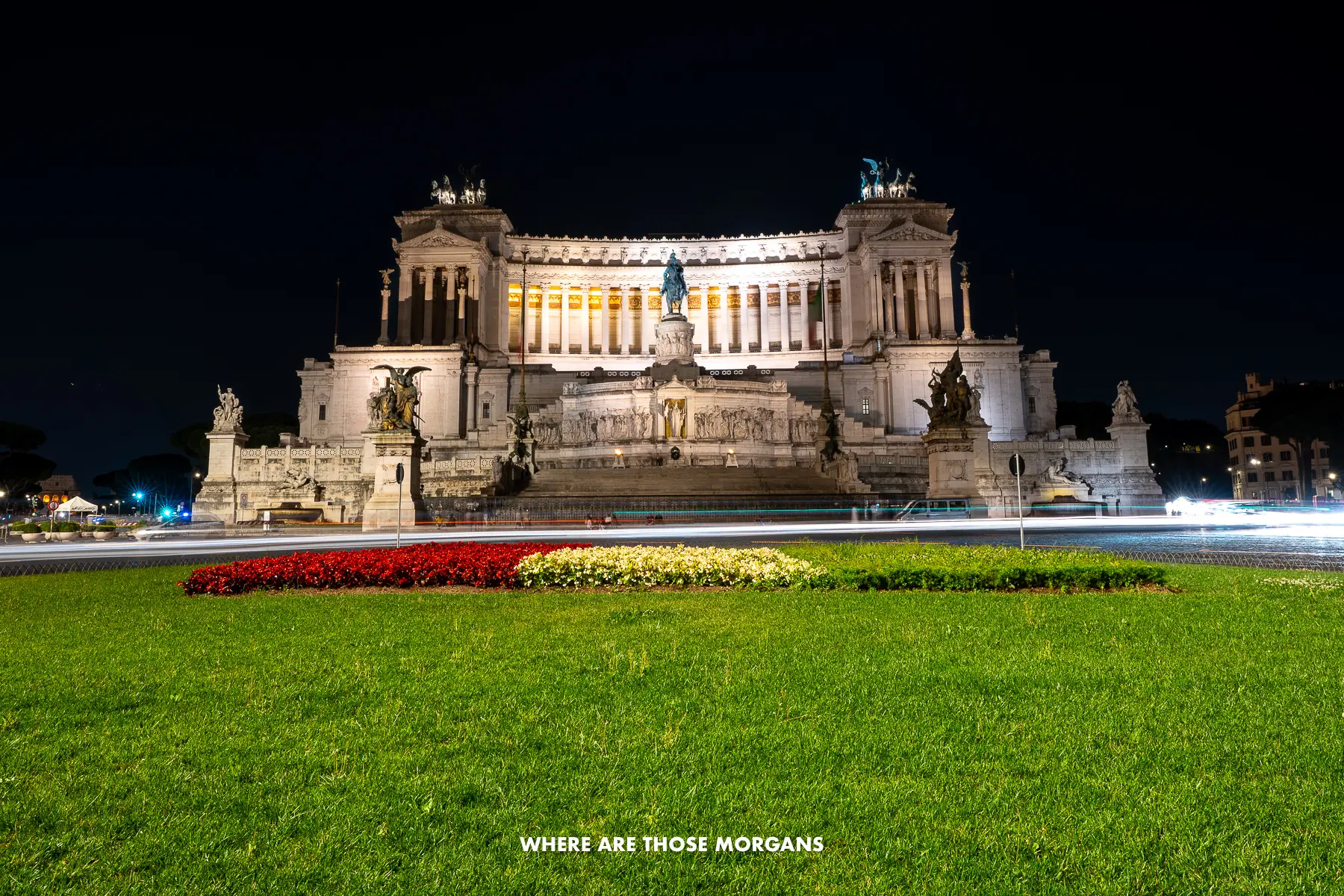 Grass and car light trails in front of a huge marble monument in Italy at night