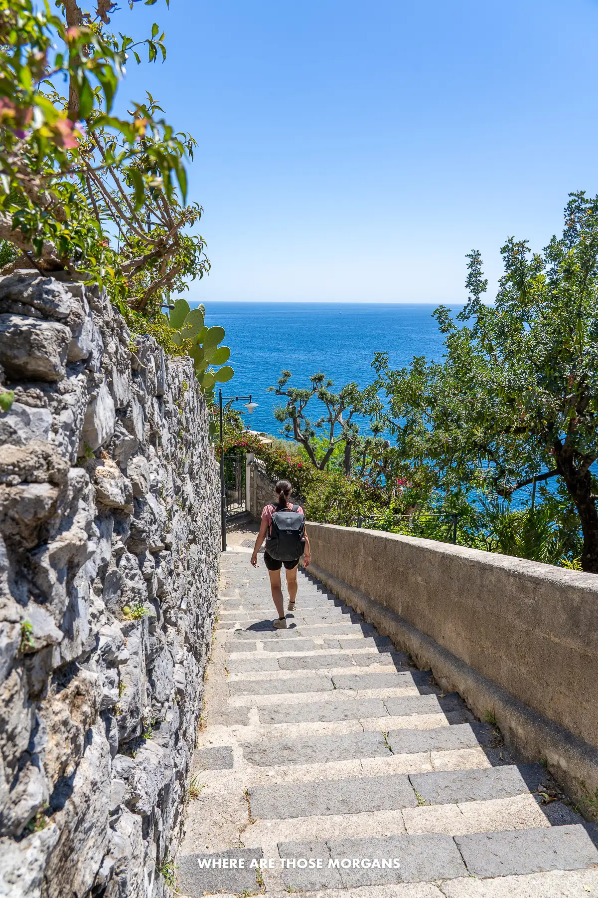 Photo of a hiker walking down steps next to a wall with views of the sea
