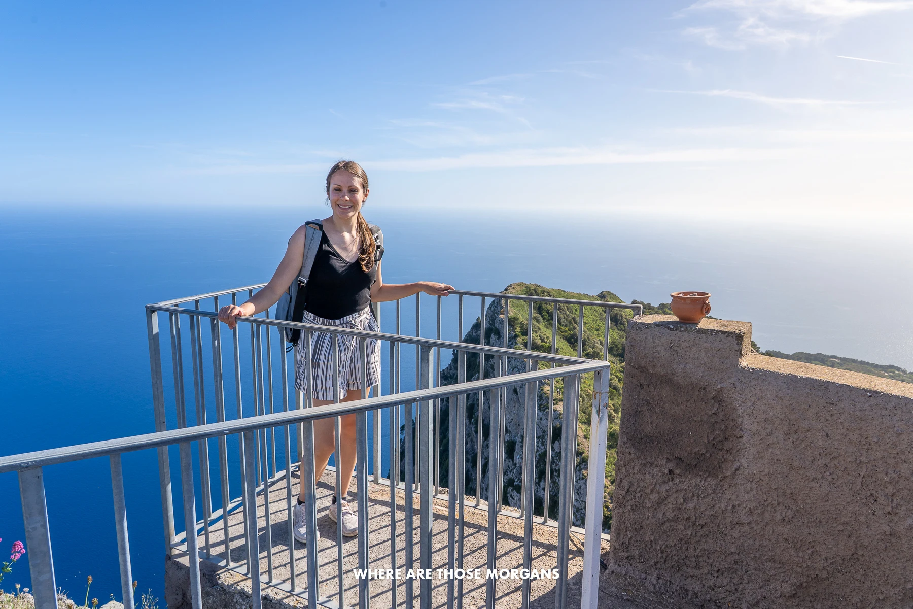 Photo of Kristen from Where Are Those Morgans standing alone on a concrete terrace with rails at the top of Monte Solaro in Capri with far reaching views of the sea behind