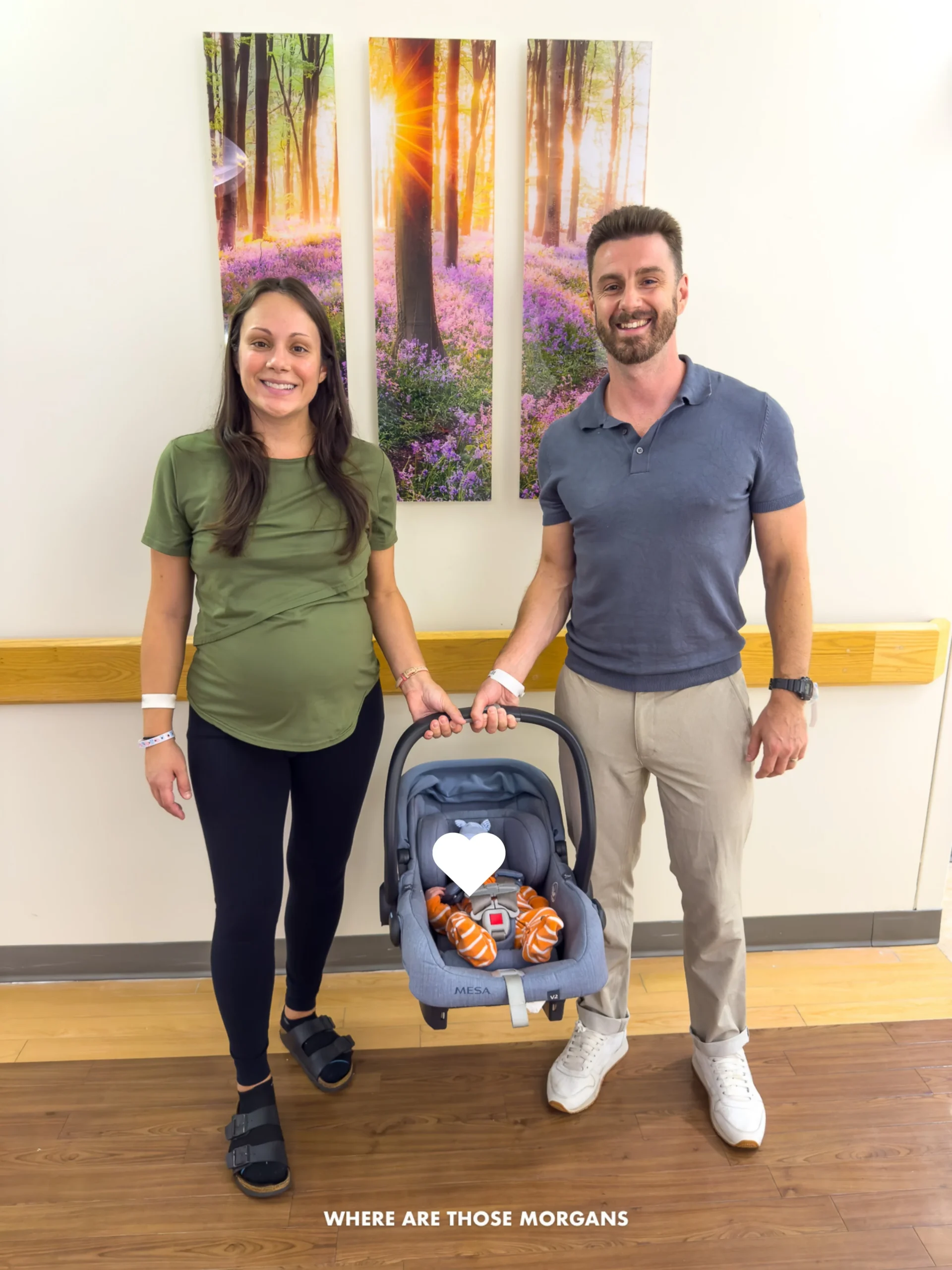Mark and Kristen Morgan from Where Are Those Morgans holding a car seat together with newborn son in 2026 in front of a three paneled photo on a wall in a maternity ward