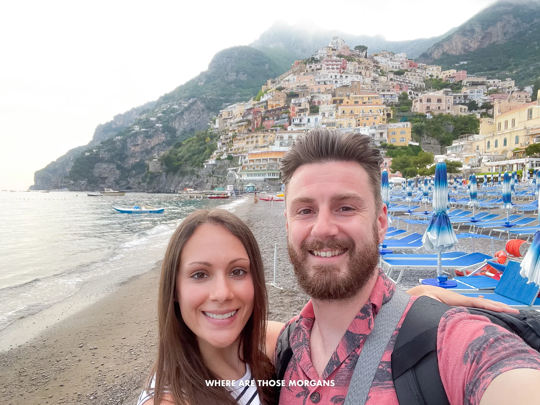 Photo of Mark and Kristen Morgan from Where Are Those Morgans taking a selfie on Positano beach at dusk with no people on the beach and heavy clouds covering the cliffs