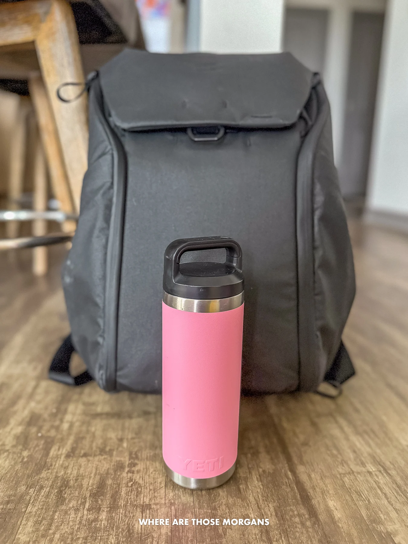 A pink Yeti water bottle against a black backpack in a kitchen