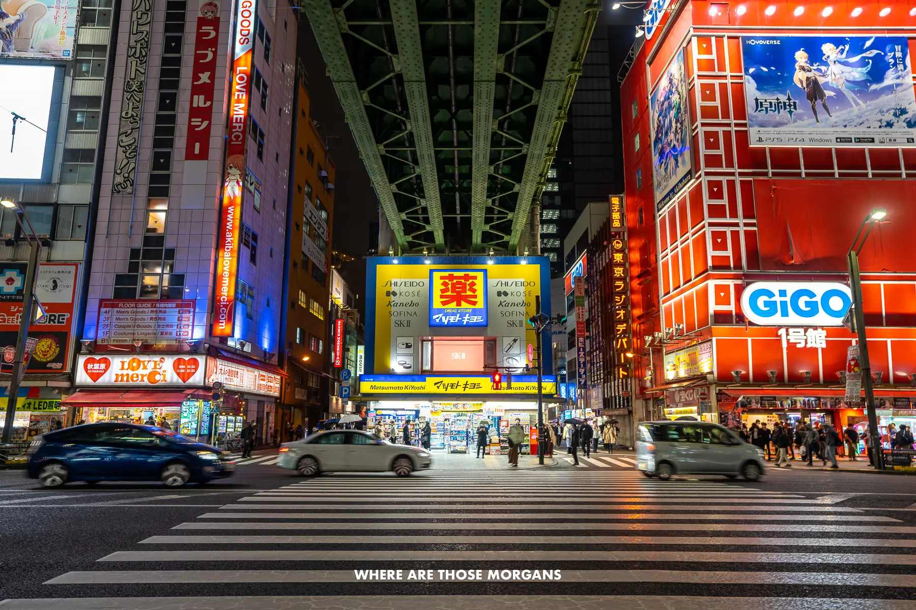 Pedestrian crossing leading to neon lit buildings next to a bridge at night in Tokyo, Japan