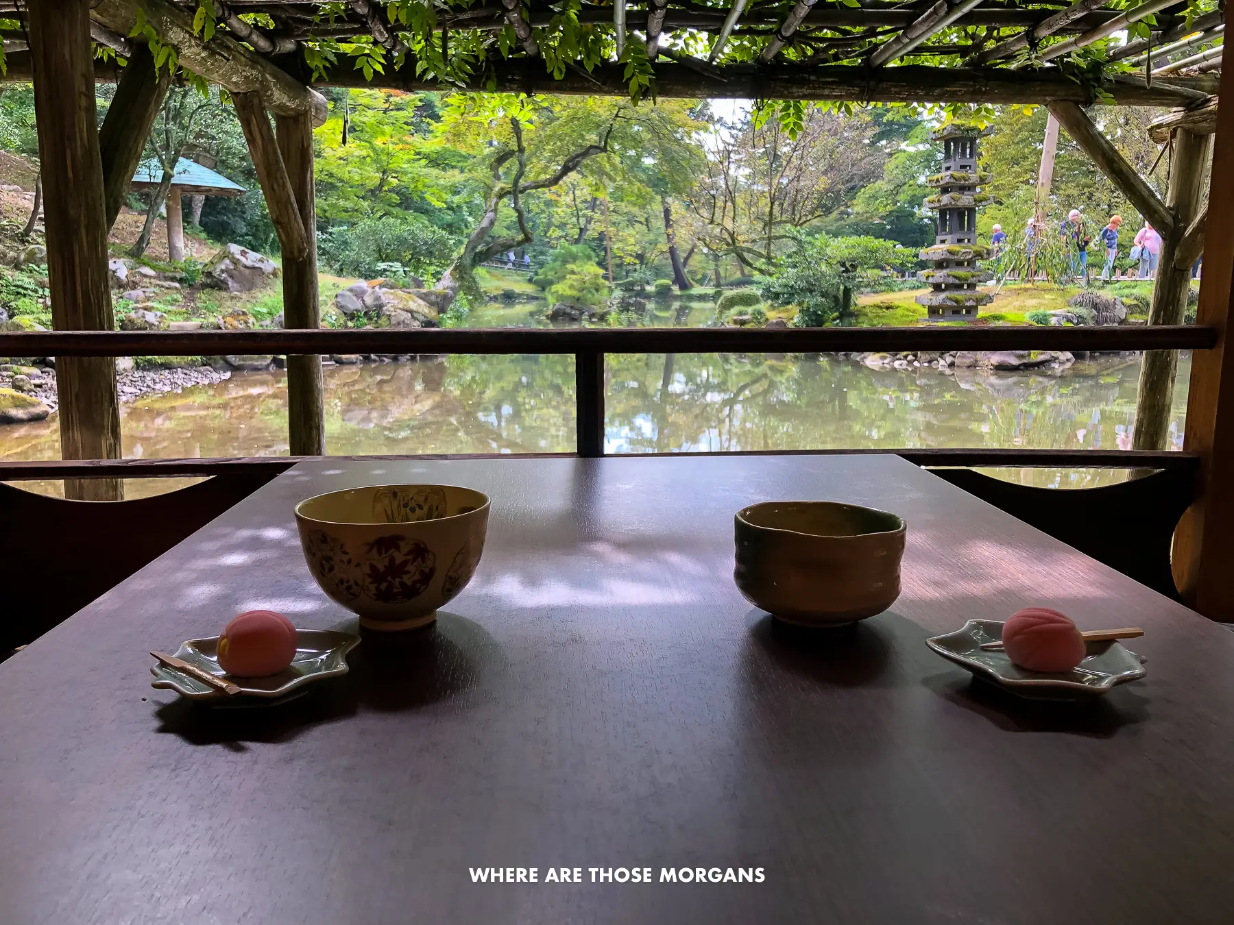 Two tea cups and sweets on a low table with views over a pond in a garden in Kanazawa