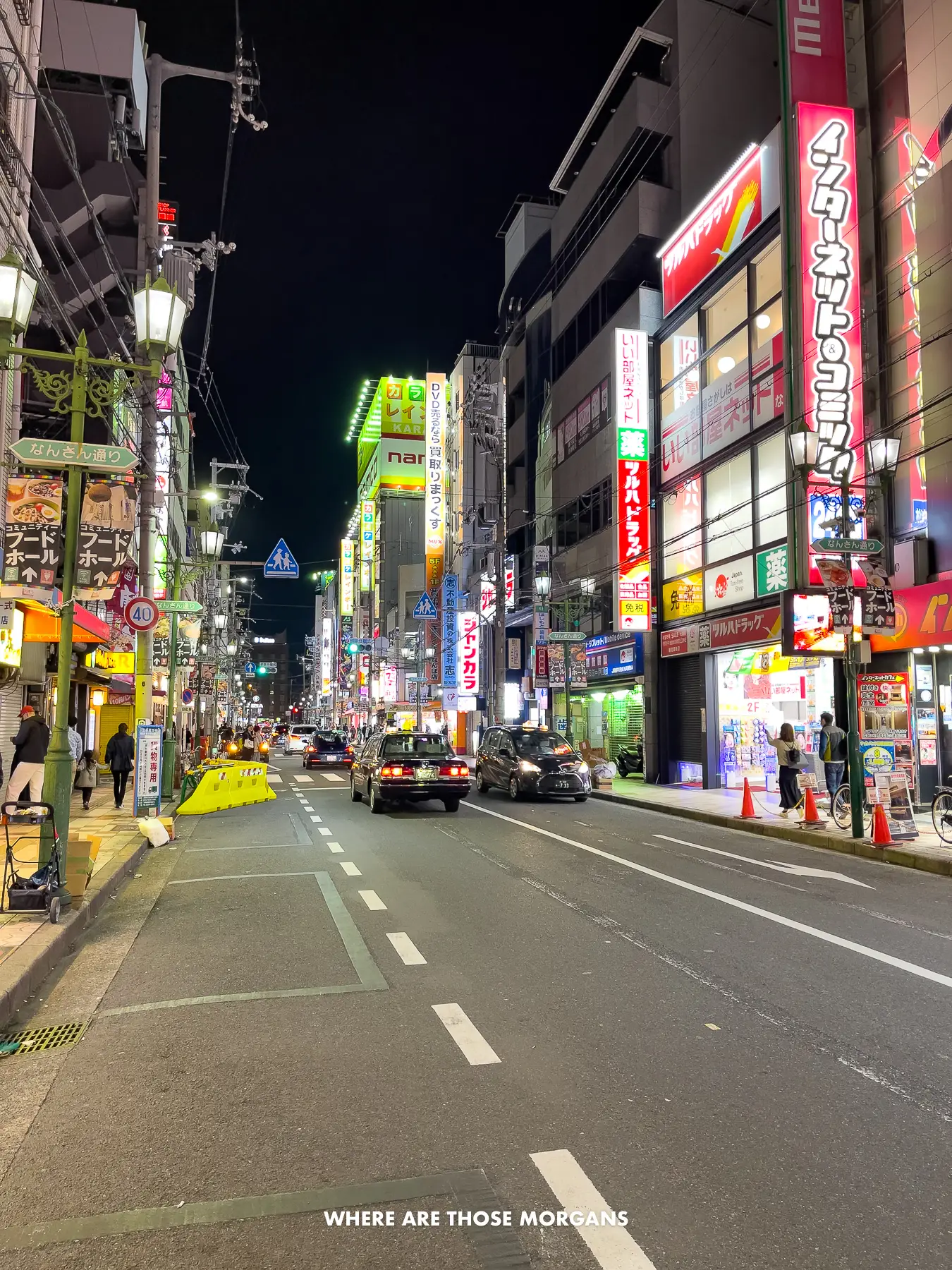 Street in Namba Osaka at night with cars and people going between buildings with neon lights