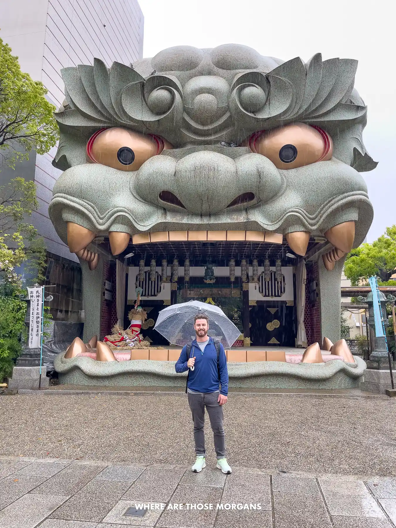 Mark from Where Are Those Morgans holding an umbrella in front of a massive lion's mouth Shinto shrine in Osaka on a rainy day