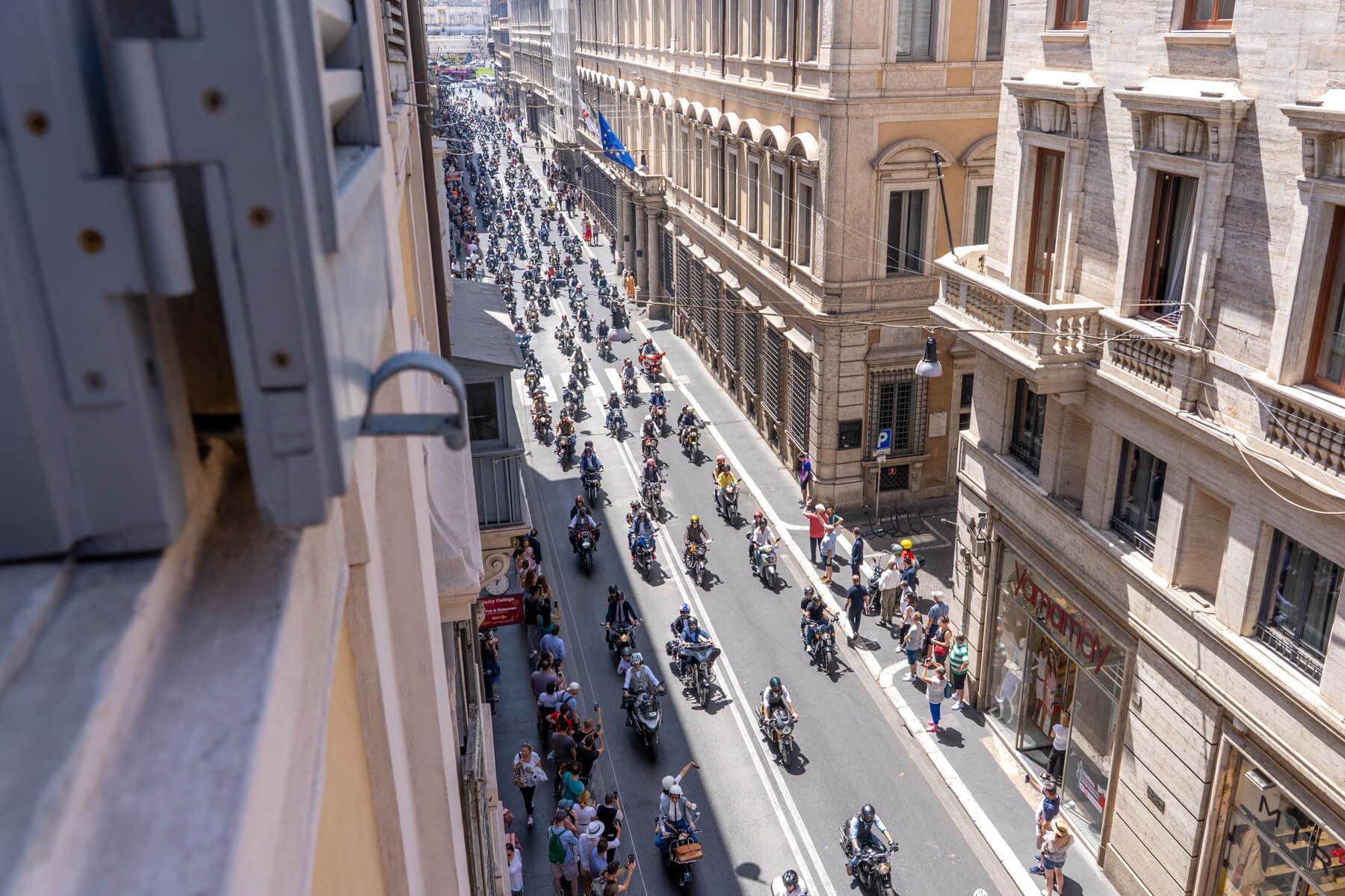 Photo looking out of a high up window in a building overlooking a road with lots of motorcycles driving along