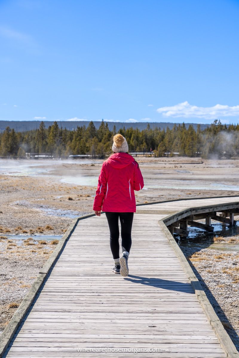 Hiker in winter clothing walking along a raised wooden boardwalk through a volcanic landscape on a sunny day but cold day
