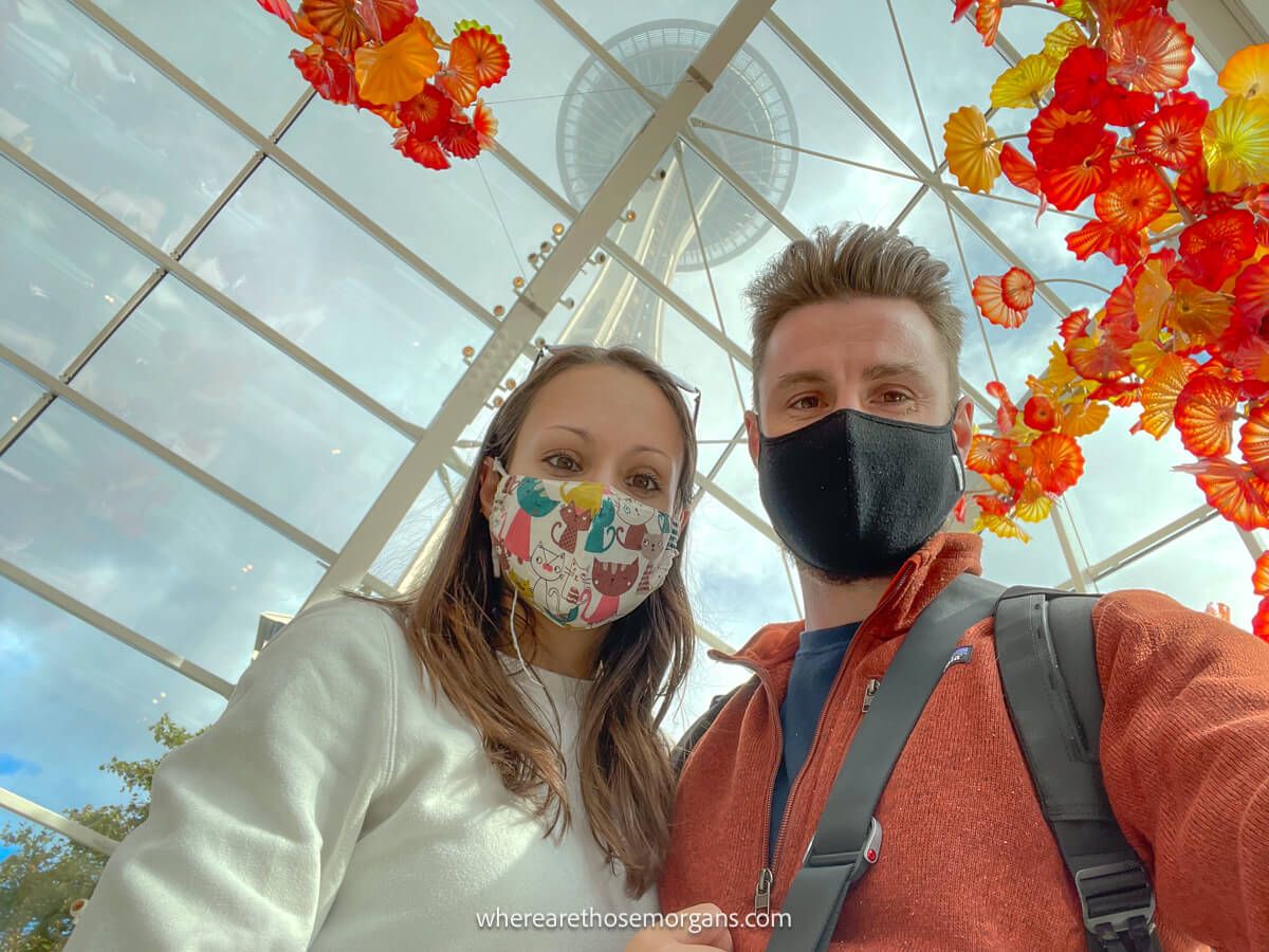 Two people taking a photo with large orange glass sculptures and the Space Needle