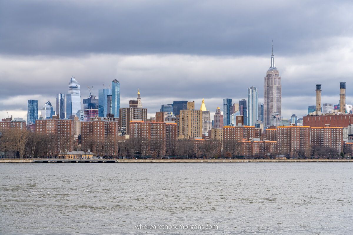 Photo of a wide river leading to high rise apartment buildings and New York City's famous skyscraper skyline on a cloudy day