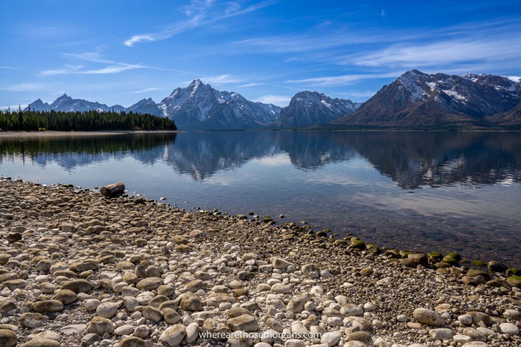 Mountains reflecting a lake next to a stone beach in Wyoming