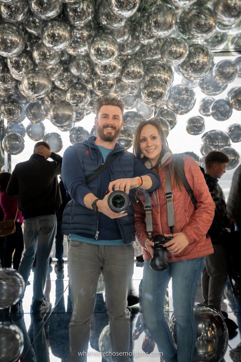 Couple taking photo in mirror with cameras and silver balloons in background