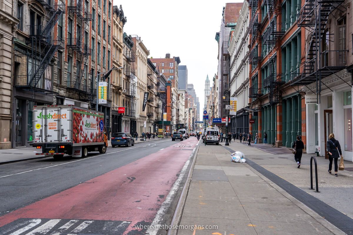 Photo of a city street with rows of buildings on either side, cars on the road and pedestrians walking on sidewalks
