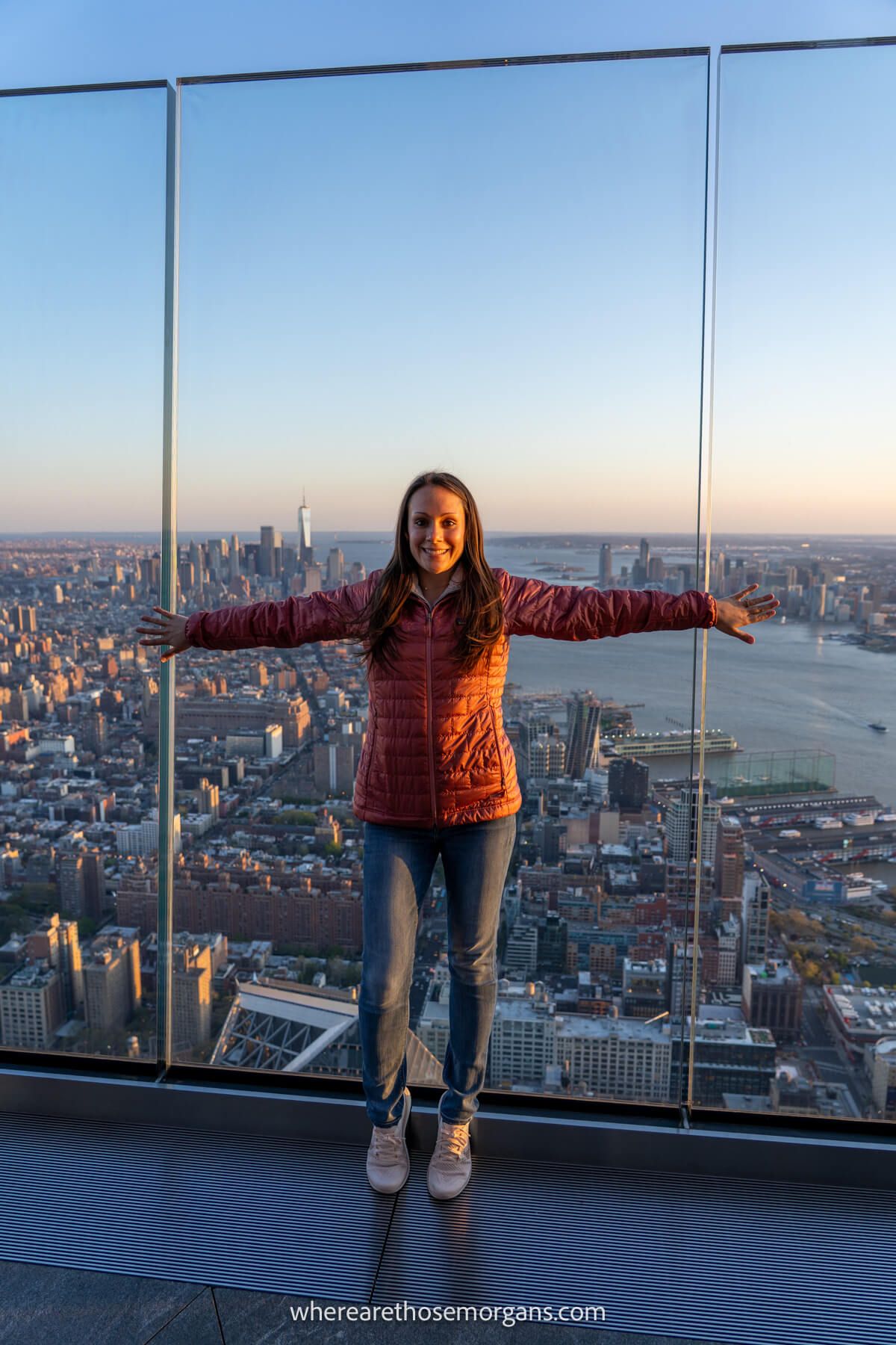 Photo of Kristen Morgan from Where Are Those Morgans standing on the Edge NYC observation deck with arms in the air and views over the city behind at dusk