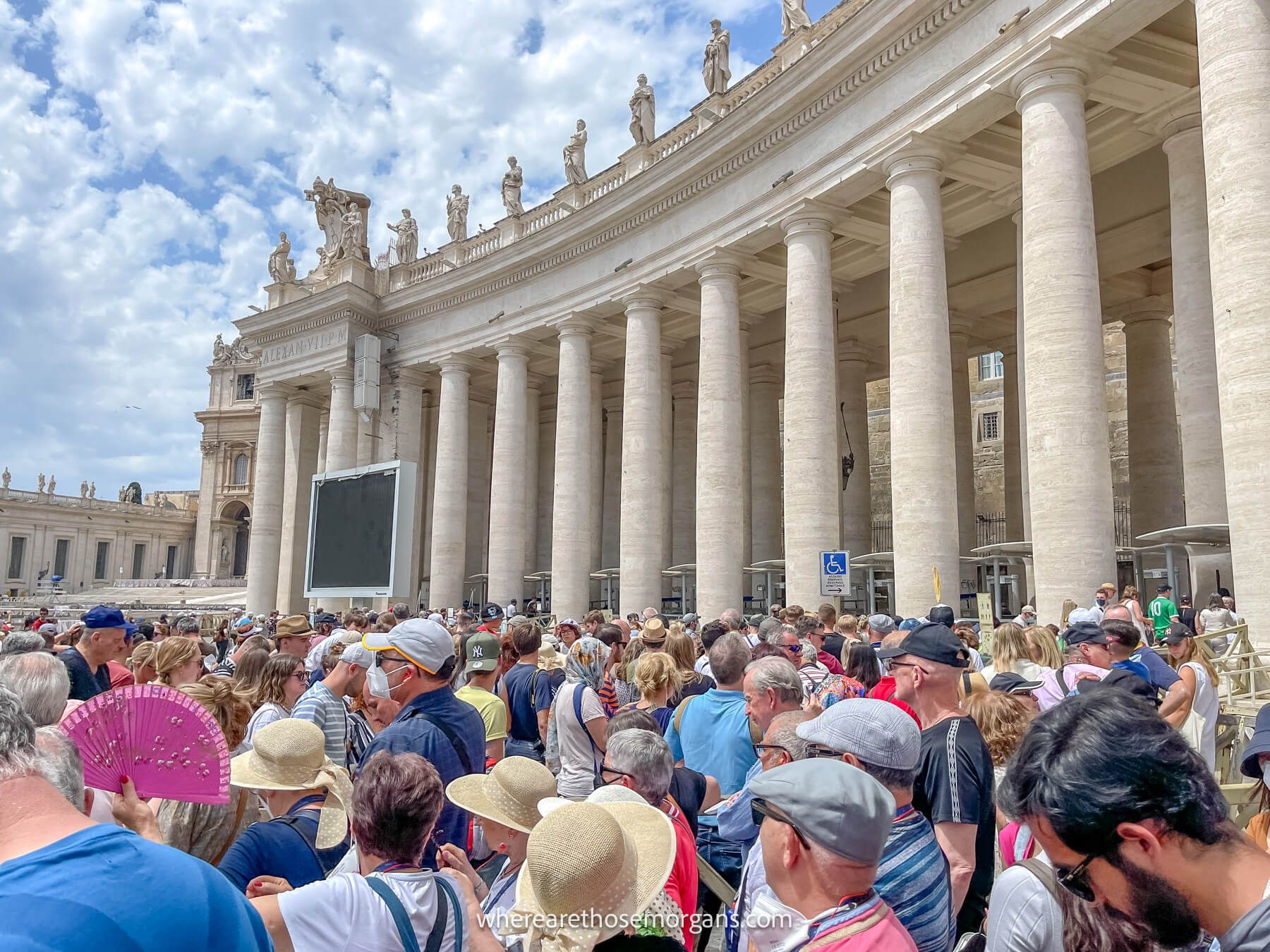 Photo of a crowd of tourists waiting in a long line to get inside a tall building with columns on a cloudy dau