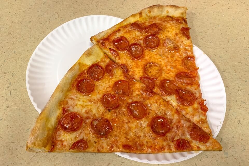 Photo of two pepperoni pizza slices on cardboard plates on a table in New York City