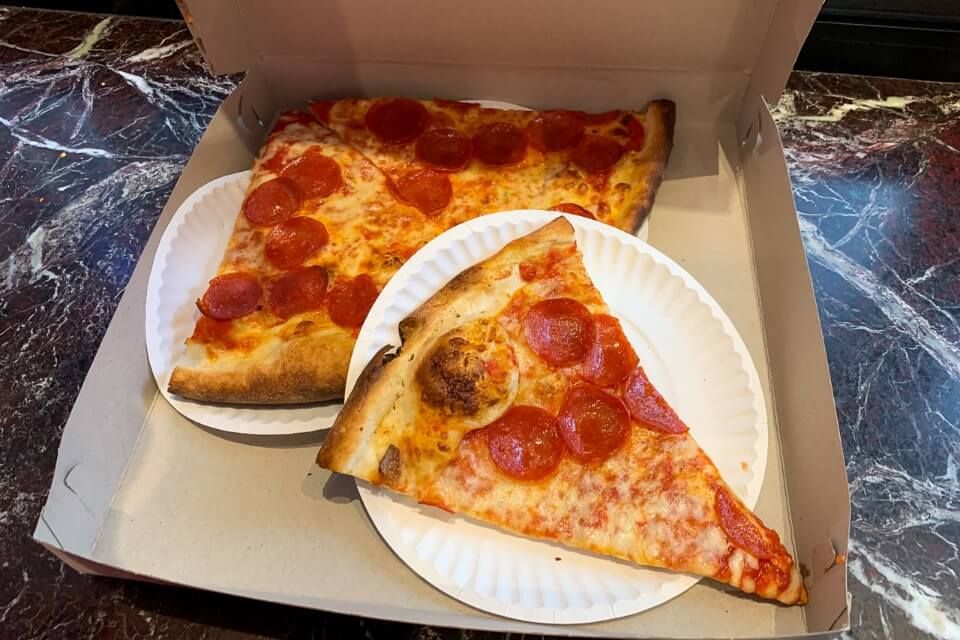 Photo of three slices of pizza inside a takeaway box on a marble table
