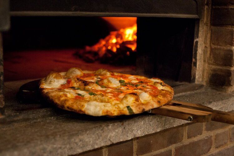 Photo of a pizza in NYC going into a large oven with fire inside