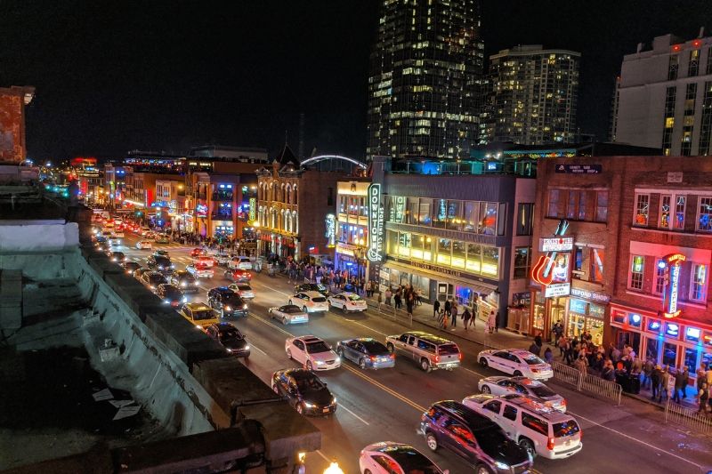 View from a roof overlooking Lower Broadway in Nashville TN with cars on the road and tourists walking between bars at night