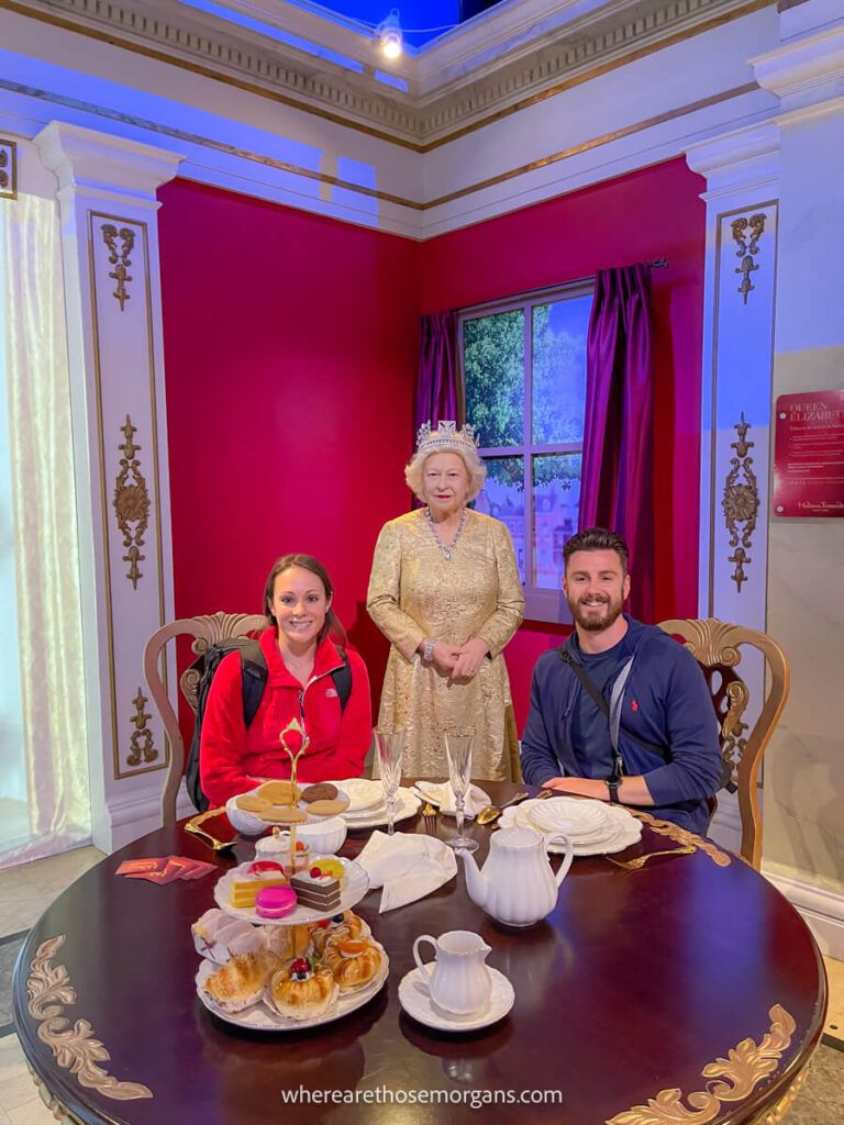 Two people sitting with a wax figure of the queen at a new York City wax museum visited with the New York Sightseeing Pass  