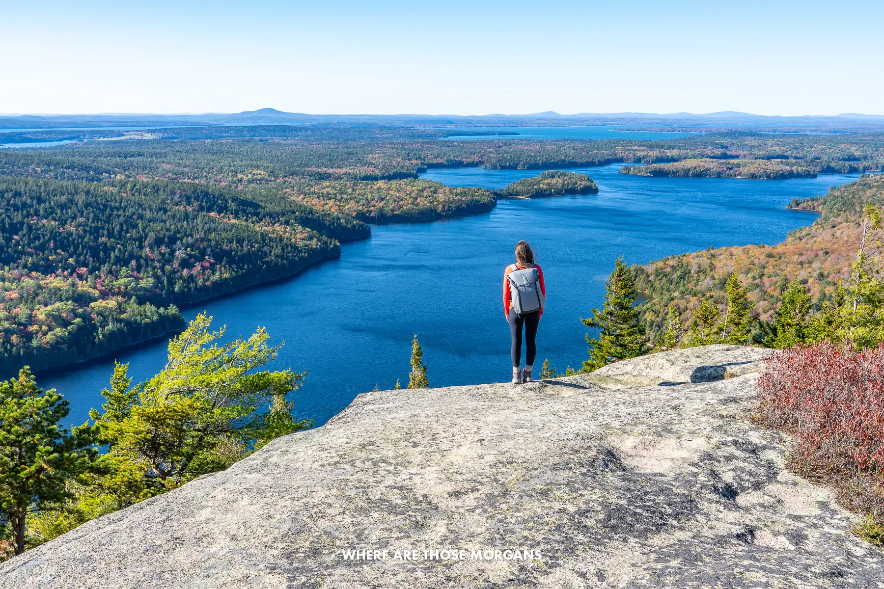 Kristen from Where Are Those Morgans standing on a granite rock looking at views over lakes and rolling hills covered in trees