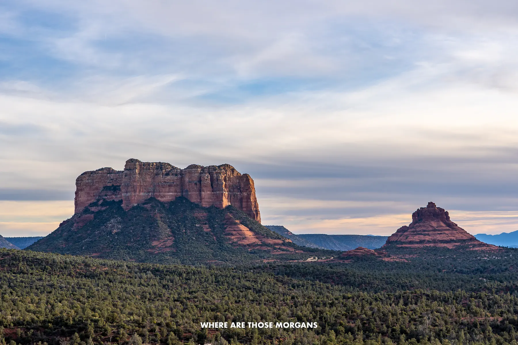 Wide open view of Bell Rock and Courthouse Butte rock formations under a colorful swirling cloud sky