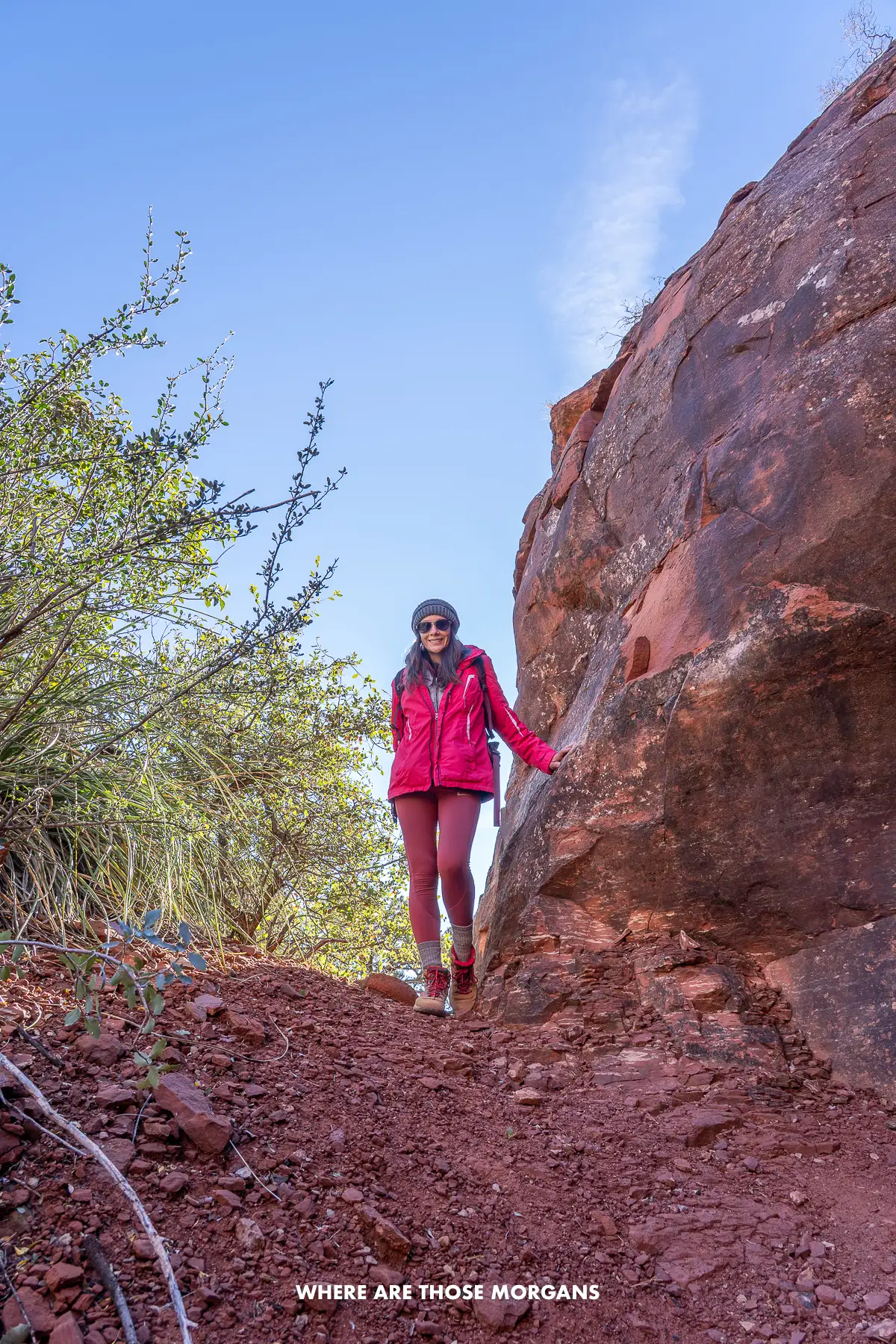 Kristen from Where Are Those Morgans leaning against a red rock next to trees on a hike in Arizona