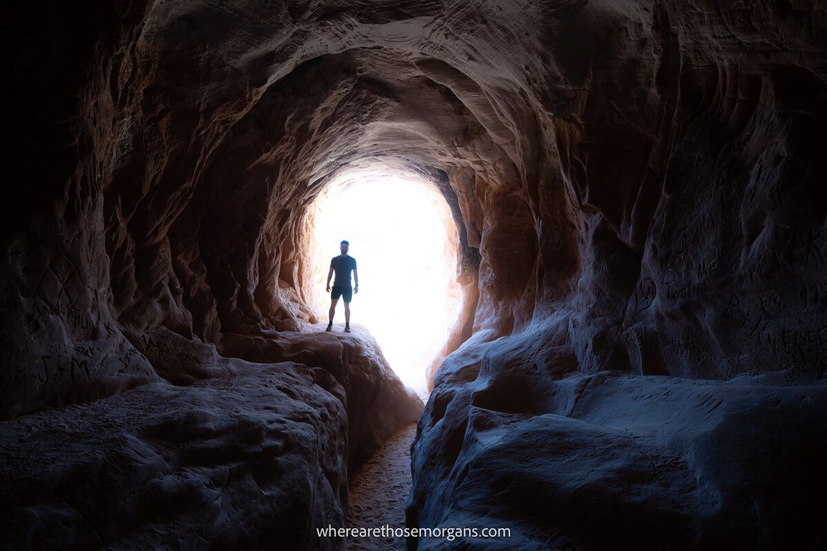 Hiker silhouetted against light at a small entrance to a tunnel
