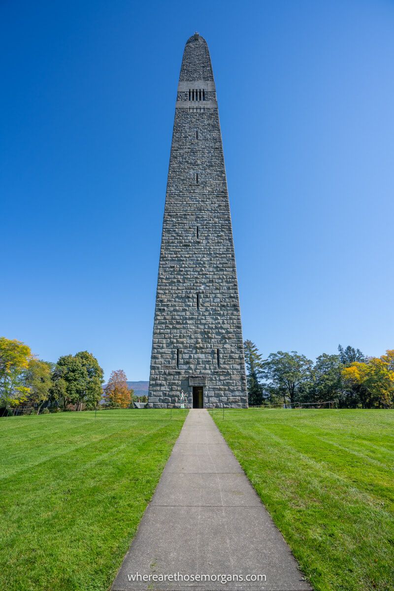 Path heading straight ahead through grass to a tall and narrow stone monument in Bennington Vermont on a sunny day