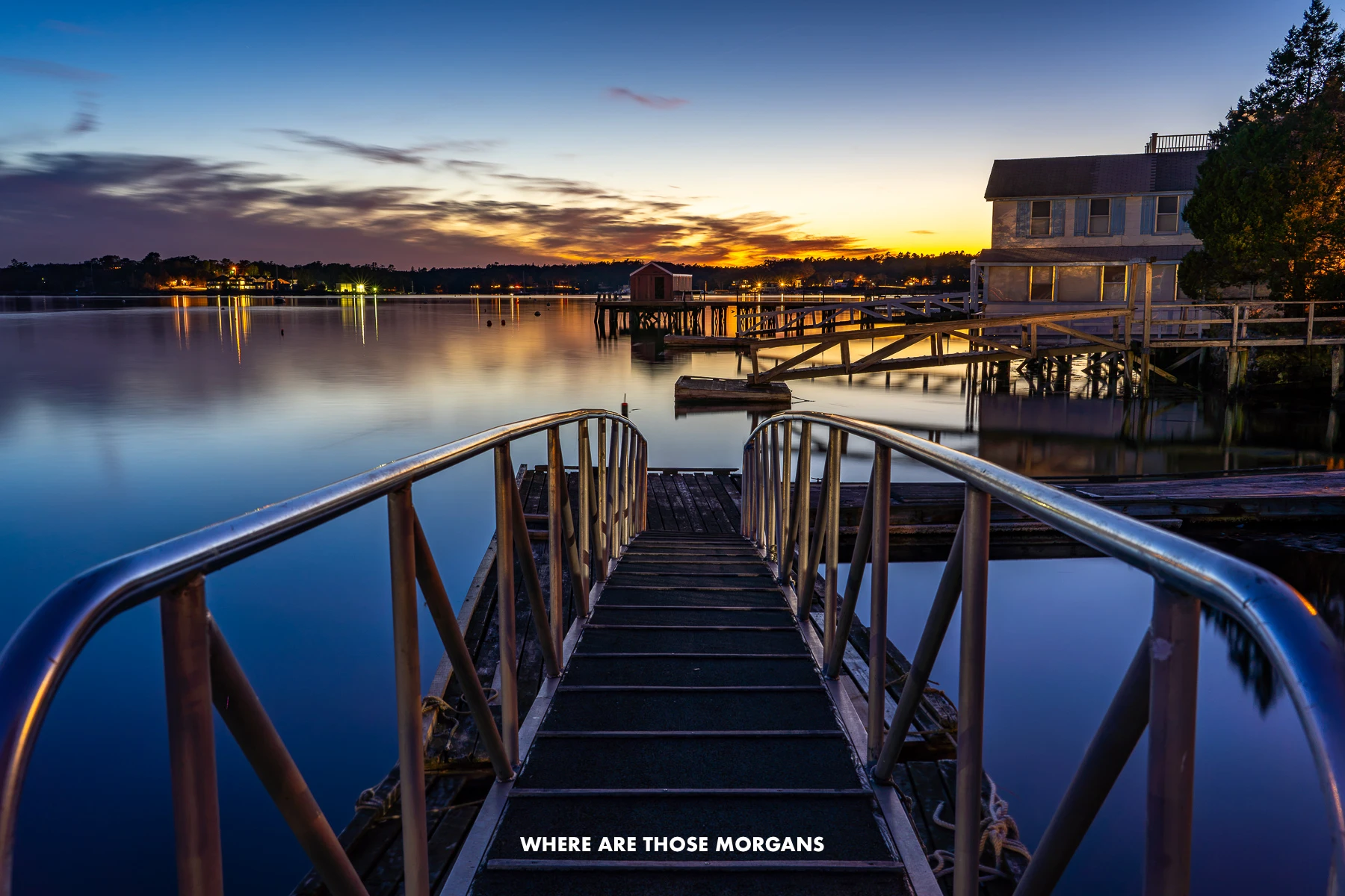 Wooden pier with metal rails leading to a perfectly still bay at sunset
