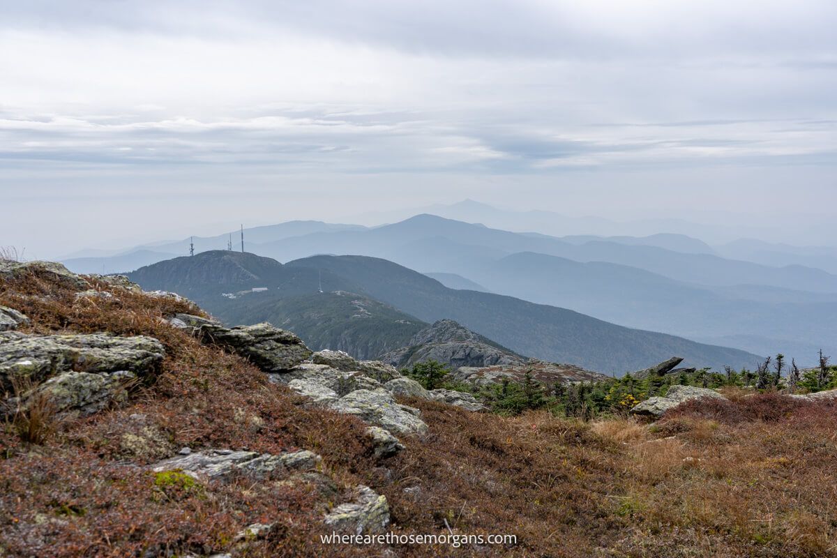 Far reaching view from the top of a mountain overlooking lots of other mountains covered in haze on a cloudy day