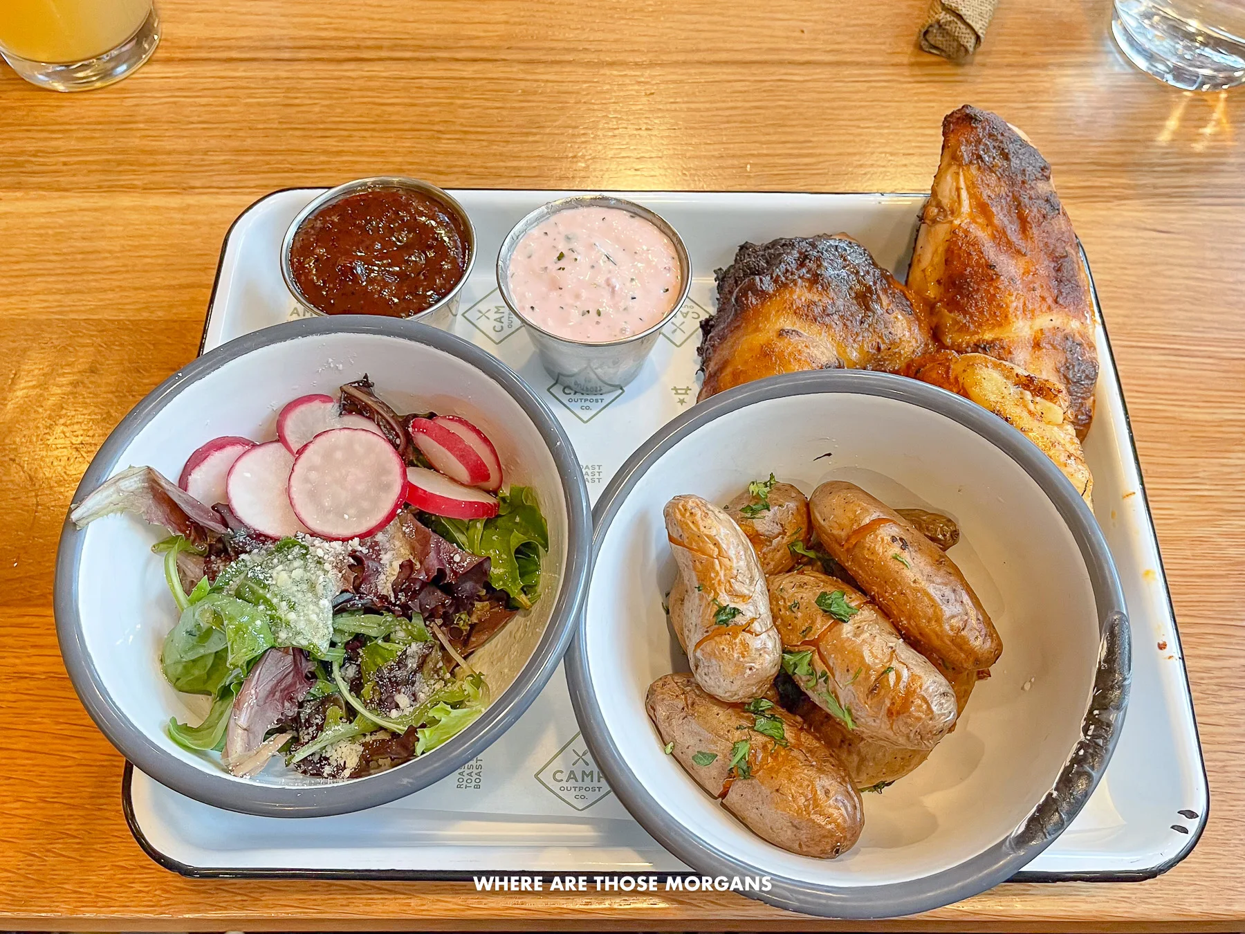 Photo of a tray on a table with bowls of potatoes, salad and chicken with dips