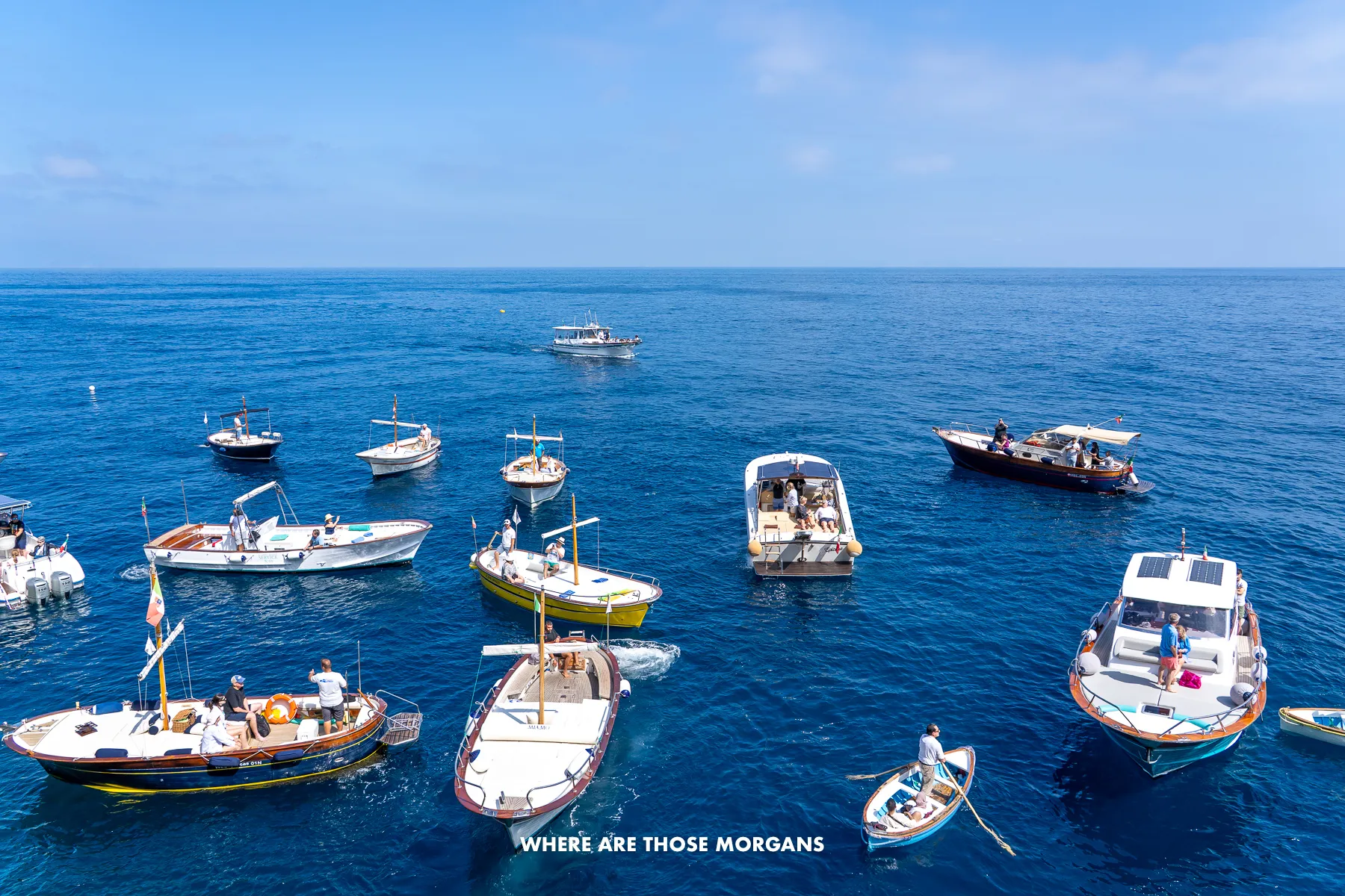 Several small boats floating near a cave in Capri with people on board waiting to be picked up by rowing boats to go inside the Blue Grotto