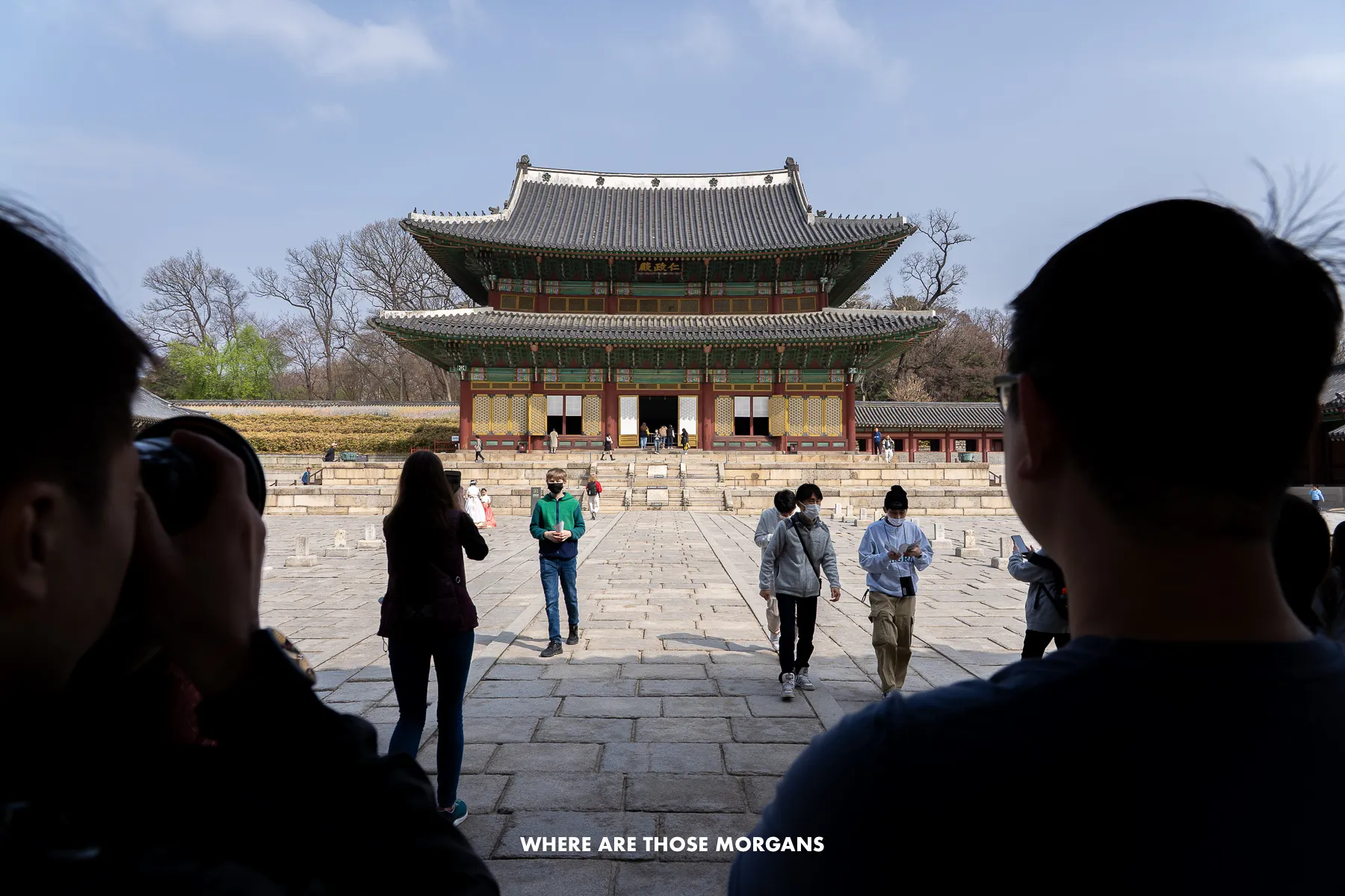 Palace building in Seoul with tourists taking photos and silhouettes of two tourists in the immediate foreground