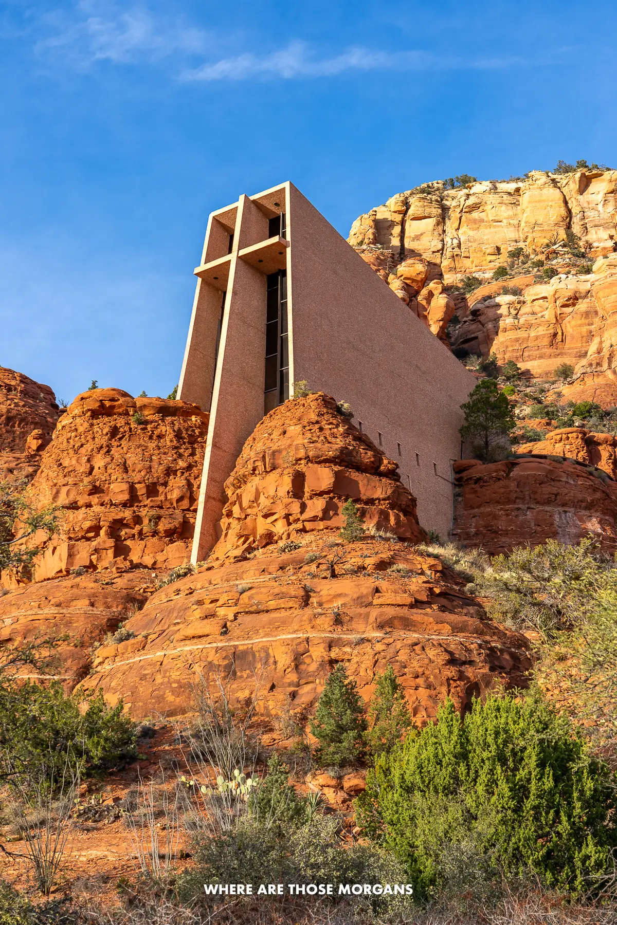 Looking up at Chapel of the Holy Cross church built into red rock cliffs with a blue sky behind