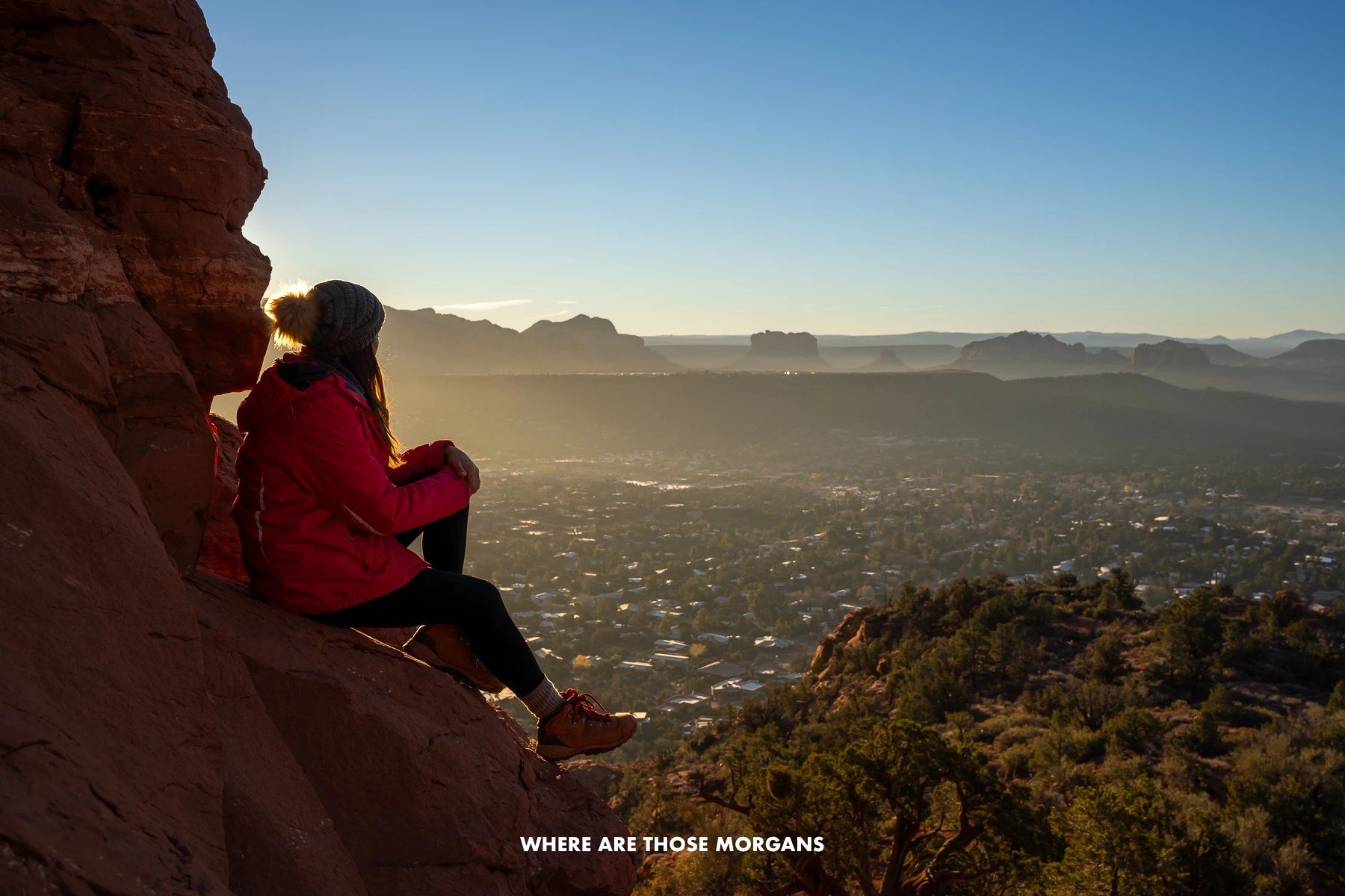 Kristen from Where Are Those Morgans sat on a red rock cliff looking at views over West Sedona at sunrise
