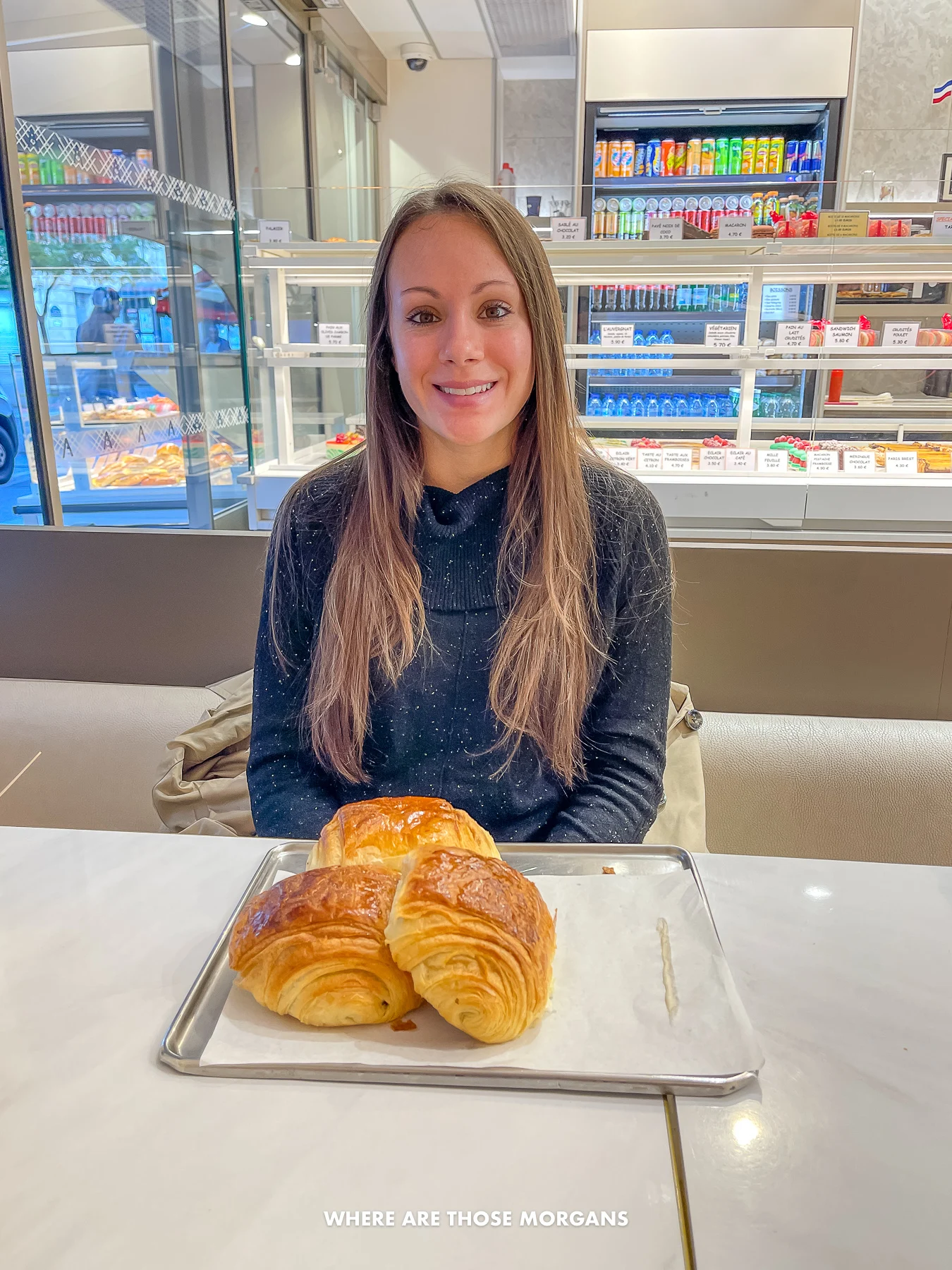 Photo of Kristen Morgan sat at a table in a low key boulangerie in Paris eating croissants