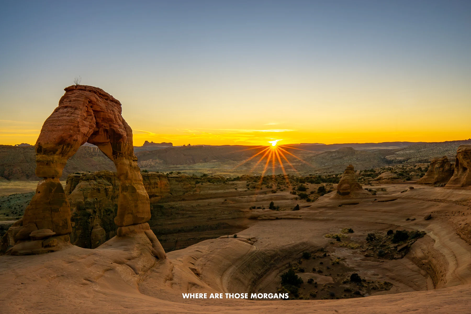 Red rock landscape with a sandstone arch formed next to a bowl-shaped depression at sunset