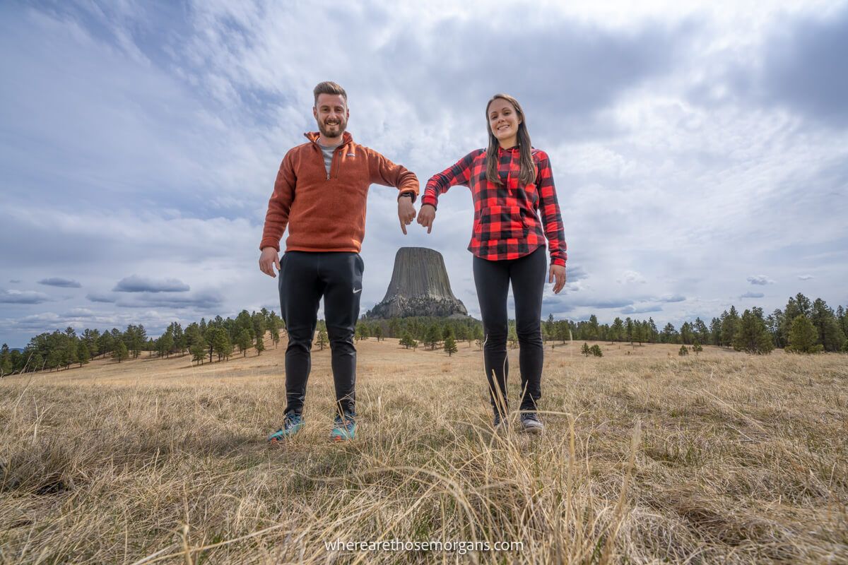 Photo of a couple standing next to each other pointing down to Devils Tower National Monument in the distance