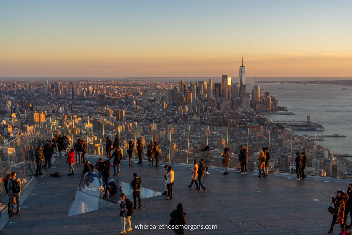 Outdoor observation deck filled with people overlooking a city skyline at sunset