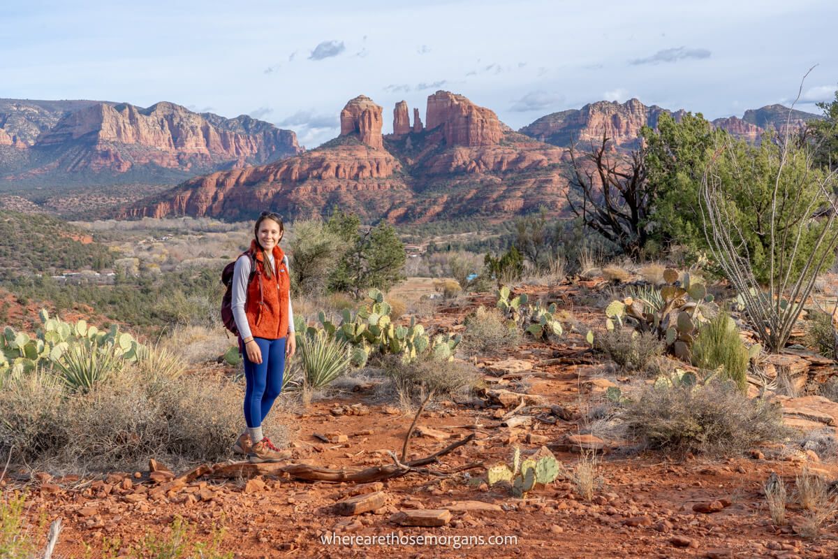 Hiker in orange vest and blue pants standing in a desert environment with vegetation and distance views over red rocks