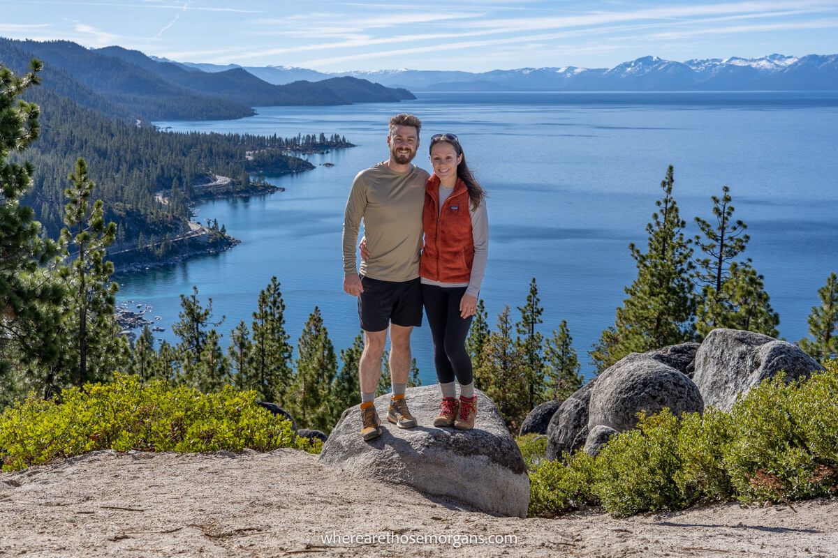 Hikers standing on a rock at a viewpoint overlooking Lake Tahoe with far reaching views of forests, roads and mountains