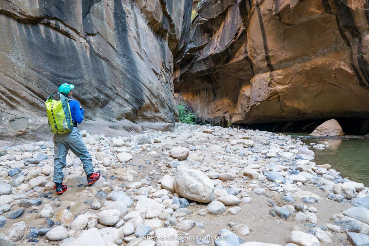 Photo of a hiker in waterproof gear standing on a rocky path next to a river inside a slot canyon in Utah