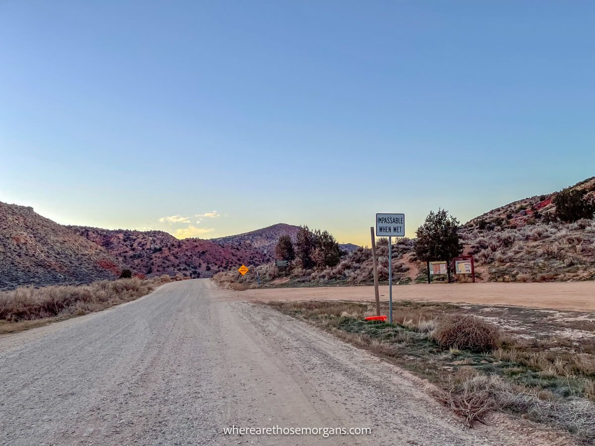 Photo of a gravel road cutting through a red rock canyon with a sign stating impassable when wet